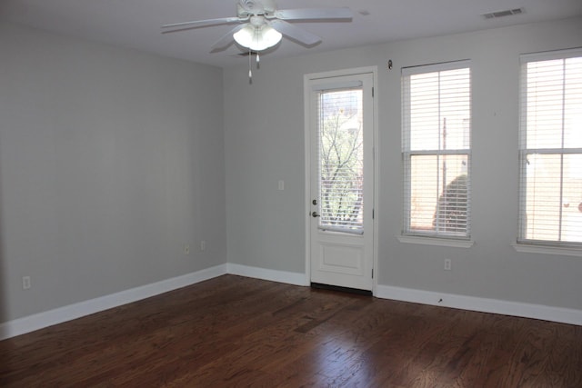 empty room with dark wood-style floors, visible vents, baseboards, and a ceiling fan