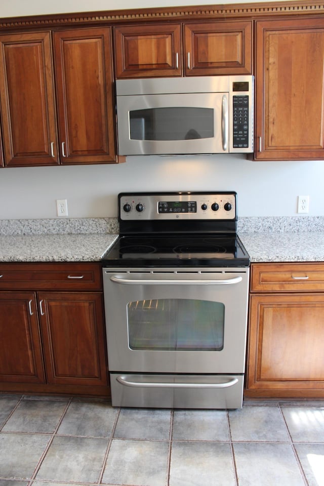 kitchen with appliances with stainless steel finishes, brown cabinetry, and light stone counters