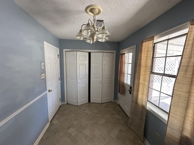 interior space with a closet, baseboards, an inviting chandelier, a textured ceiling, and brick patterned floor