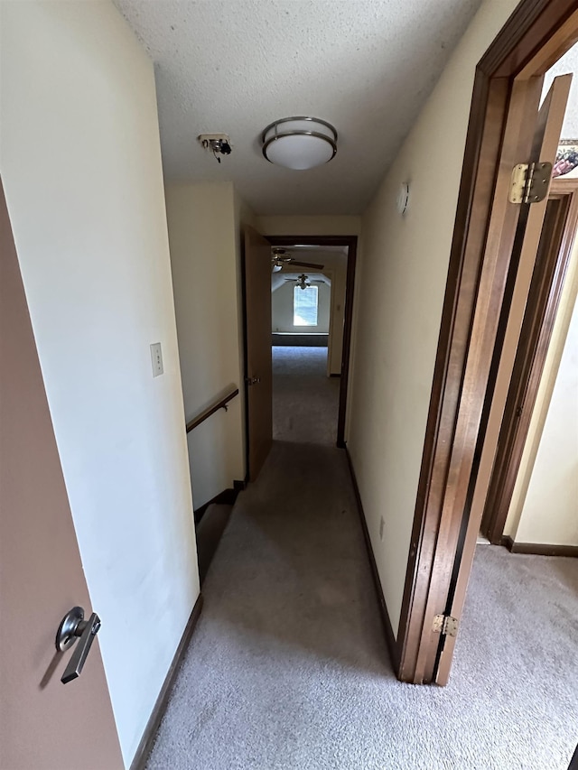 corridor with a textured ceiling, carpet floors, and baseboards