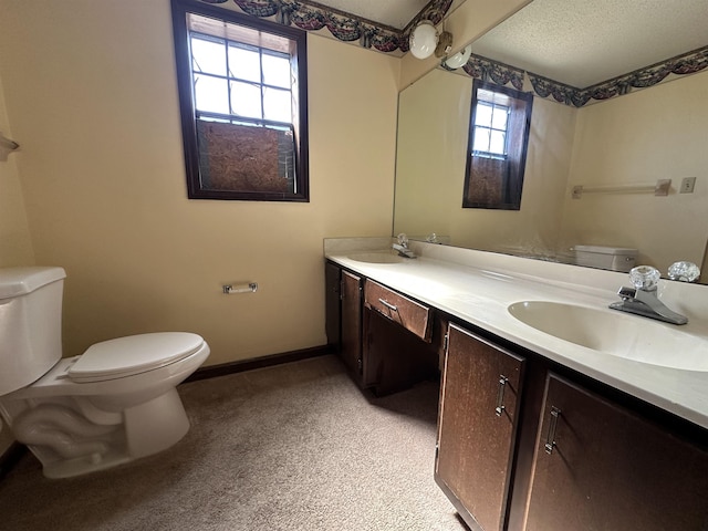 bathroom with toilet, double vanity, baseboards, and a sink