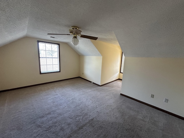 additional living space featuring a textured ceiling, carpet floors, visible vents, baseboards, and vaulted ceiling