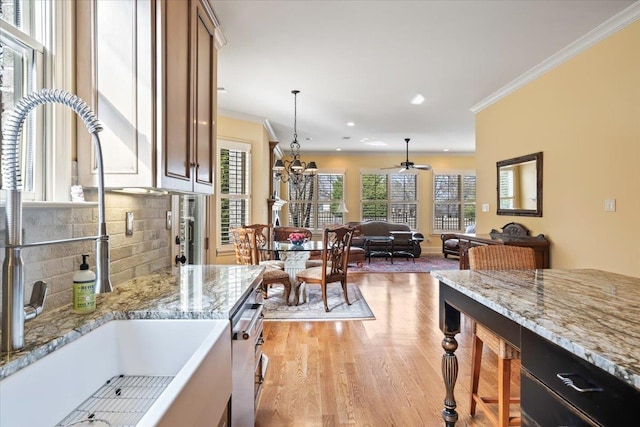 kitchen featuring light stone counters, crown molding, light wood-style flooring, decorative backsplash, and a sink