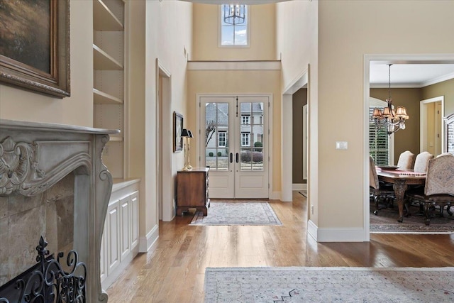 foyer with french doors, crown molding, a notable chandelier, light wood finished floors, and baseboards