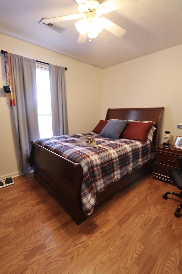 bedroom featuring a ceiling fan, visible vents, and wood finished floors