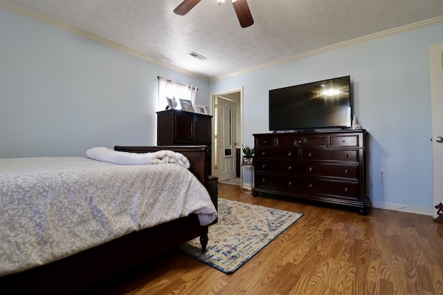 bedroom with baseboards, visible vents, ornamental molding, wood finished floors, and a textured ceiling