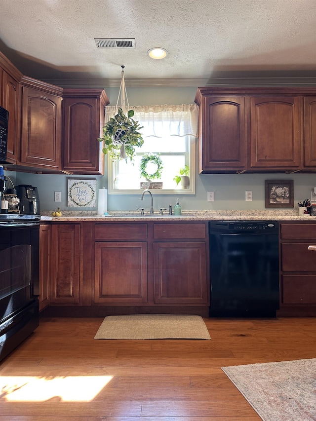 kitchen featuring a sink, visible vents, light wood-style floors, light stone countertops, and black appliances