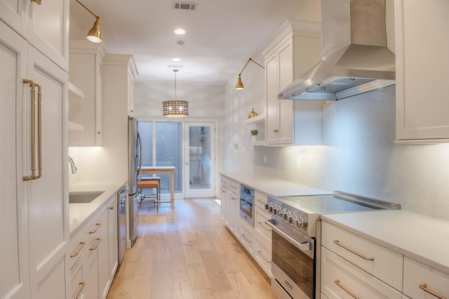 kitchen featuring a sink, light countertops, appliances with stainless steel finishes, light wood-type flooring, and wall chimney exhaust hood