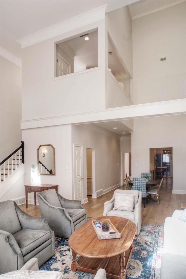 living area featuring baseboards, a towering ceiling, wood finished floors, stairs, and crown molding