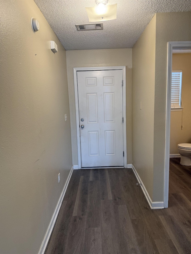 doorway featuring visible vents, a textured ceiling, baseboards, and dark wood-type flooring