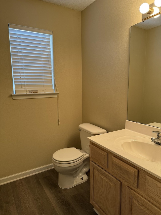 half bath with baseboards, vanity, toilet, and wood finished floors