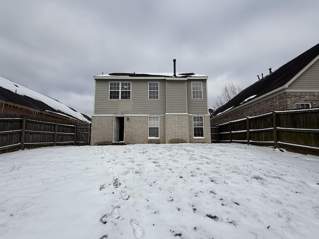 snow covered back of property featuring brick siding and a fenced backyard