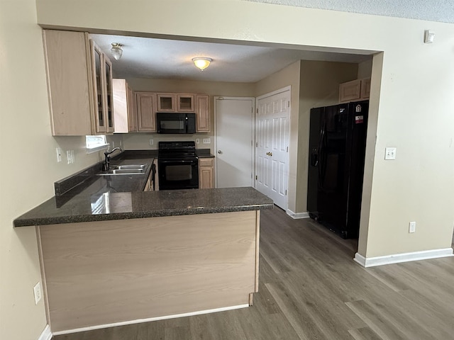 kitchen featuring a peninsula, wood finished floors, a sink, baseboards, and black appliances