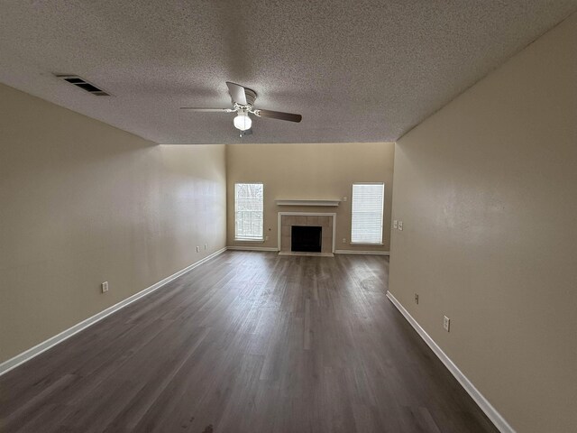 unfurnished living room with ceiling fan, a tile fireplace, visible vents, baseboards, and dark wood finished floors