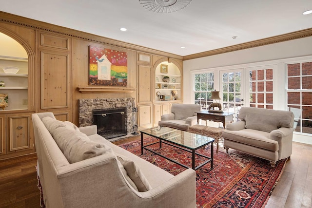 living room with dark wood-type flooring, a stone fireplace, crown molding, french doors, and built in shelves