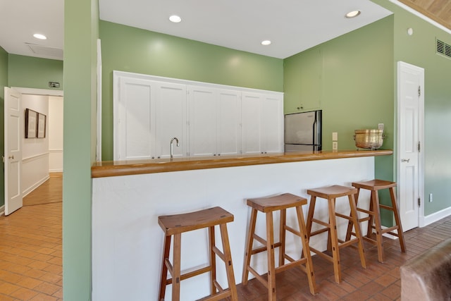 kitchen featuring brick floor, recessed lighting, visible vents, a kitchen breakfast bar, and freestanding refrigerator