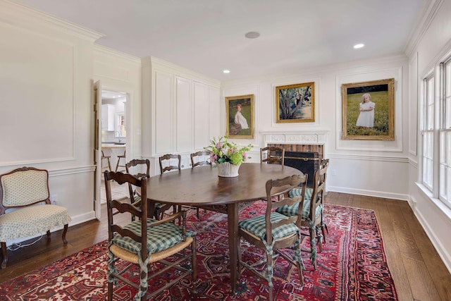 dining area with a decorative wall, dark wood-type flooring, baseboards, a brick fireplace, and crown molding