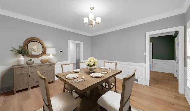 dining space with a chandelier, wainscoting, light wood-style flooring, and crown molding