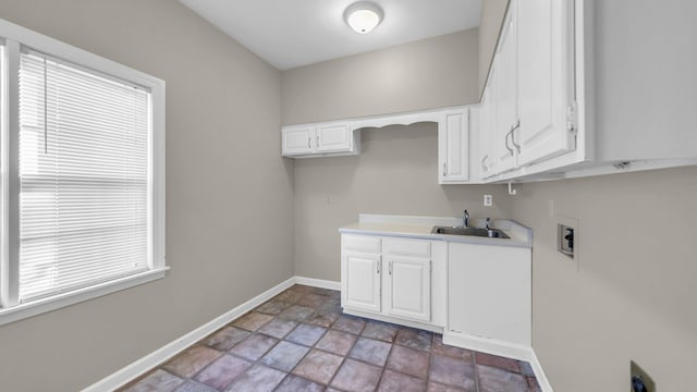 laundry area featuring washer hookup, cabinet space, stone finish floor, a sink, and baseboards