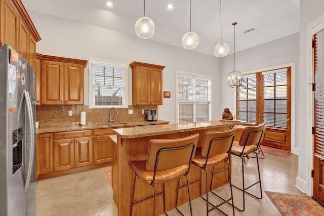 kitchen featuring light stone counters, visible vents, backsplash, a sink, and stainless steel fridge with ice dispenser