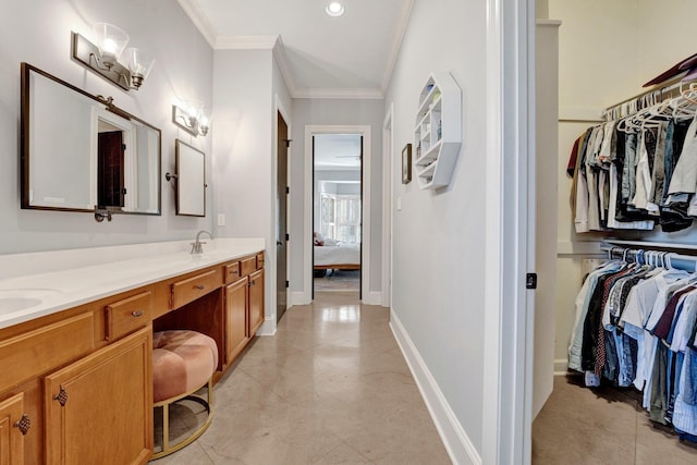 ensuite bathroom with a walk in closet, crown molding, baseboards, and double vanity