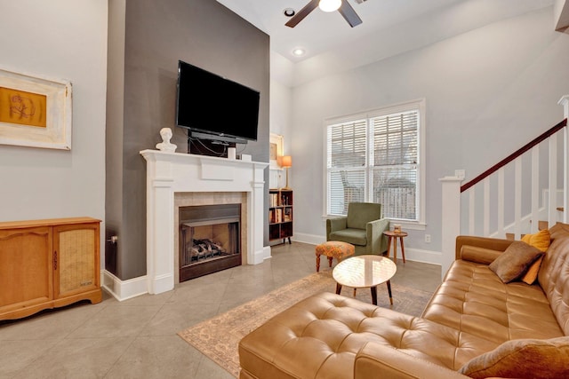 living room with ceiling fan, light tile patterned flooring, a tile fireplace, baseboards, and stairway