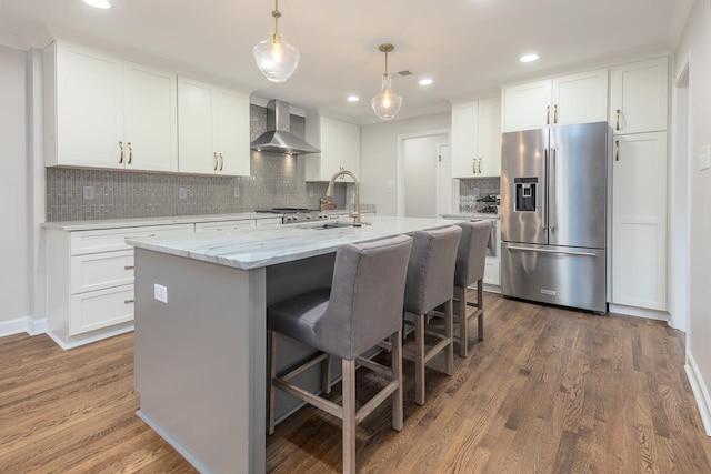 kitchen with wall chimney exhaust hood, wood finished floors, stainless steel fridge, and white cabinets