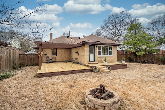 rear view of property with an outdoor fire pit, brick siding, a deck, and a fenced backyard