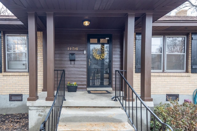 entrance to property featuring crawl space, brick siding, and covered porch