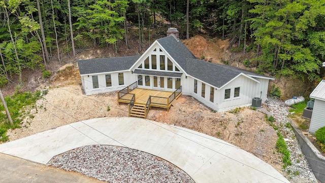 view of front facade with central AC, roof with shingles, a wooden deck, and driveway