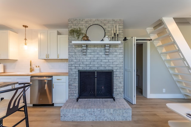 kitchen with a fireplace, white cabinets, light wood finished floors, dishwasher, and tasteful backsplash