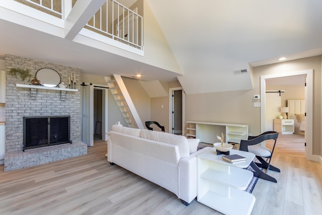 living room featuring light wood-style flooring, stairs, visible vents, and a barn door