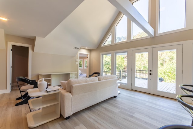 living room featuring high vaulted ceiling, french doors, light wood-type flooring, and a healthy amount of sunlight