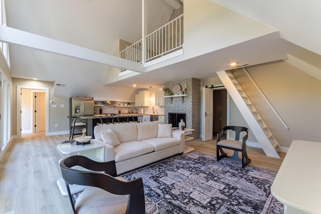 living area featuring light wood finished floors, stairway, a high ceiling, a brick fireplace, and baseboards