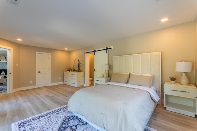 bedroom with a barn door, wood finished floors, visible vents, and baseboards