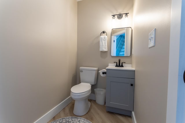 half bath with toilet, vanity, baseboards, and wood finished floors