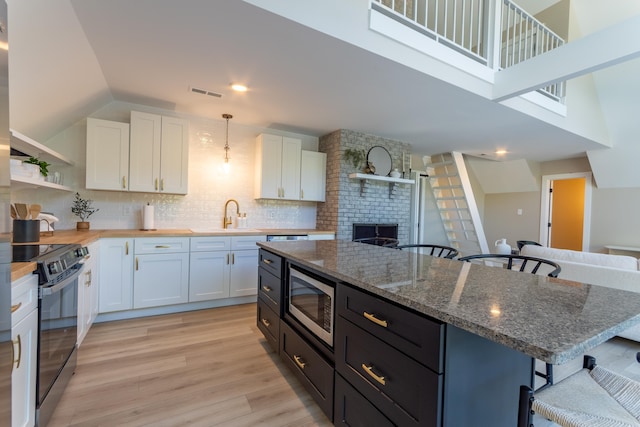 kitchen with black / electric stove, a breakfast bar, a sink, visible vents, and stainless steel microwave