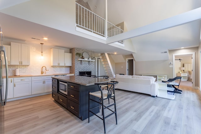 kitchen with light wood-style flooring, a kitchen breakfast bar, open floor plan, white cabinets, and stainless steel microwave