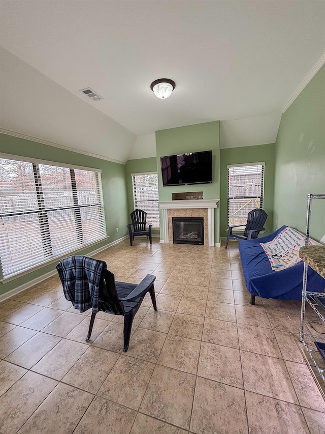 tiled living area with baseboards, visible vents, a glass covered fireplace, lofted ceiling, and ornamental molding