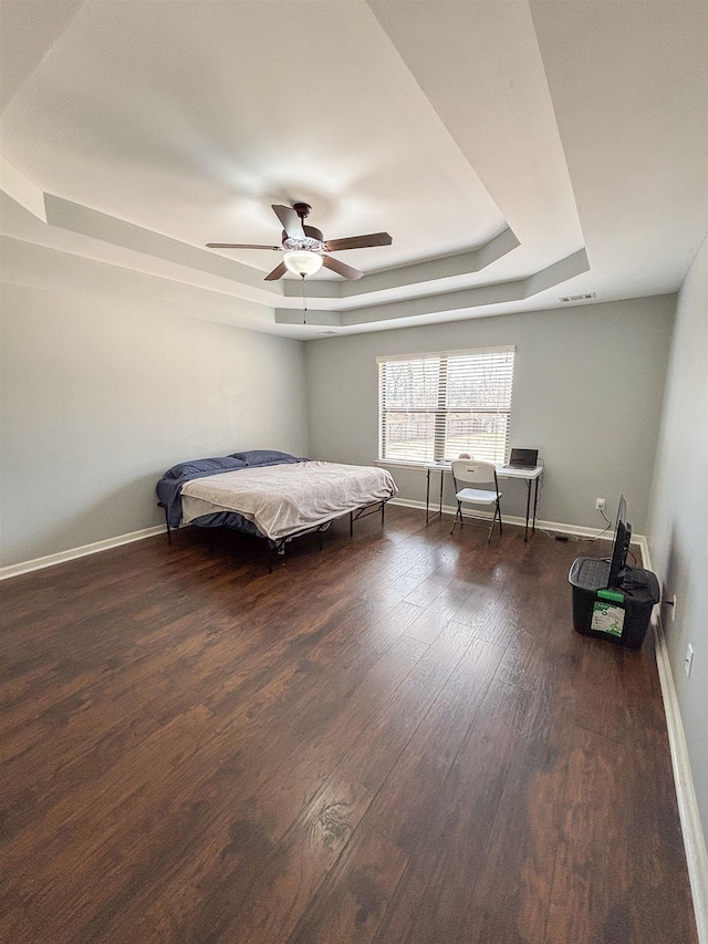 bedroom with baseboards, a tray ceiling, and wood finished floors