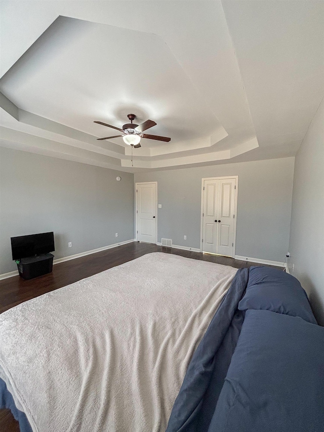 bedroom with dark wood-style flooring, a ceiling fan, visible vents, baseboards, and a raised ceiling