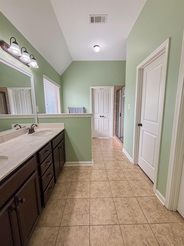 bathroom with double vanity, lofted ceiling, visible vents, a sink, and tile patterned floors