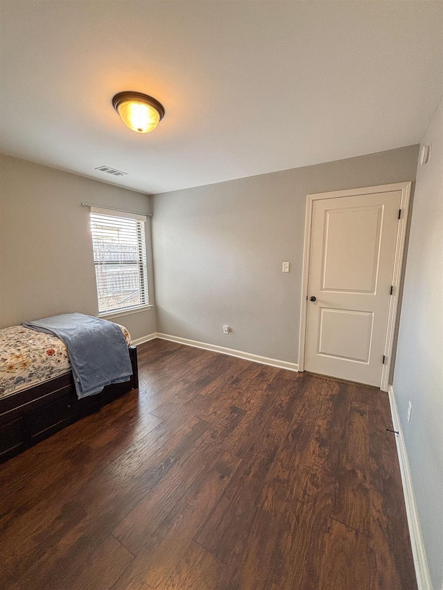 unfurnished bedroom featuring dark wood-style floors, visible vents, and baseboards