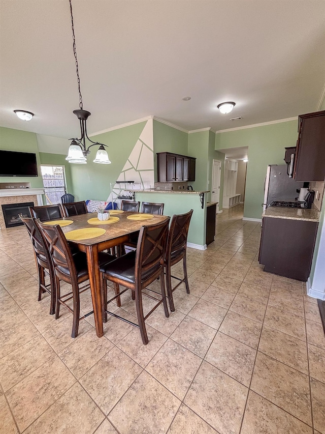 dining space featuring ornamental molding, baseboards, a tiled fireplace, and light tile patterned floors