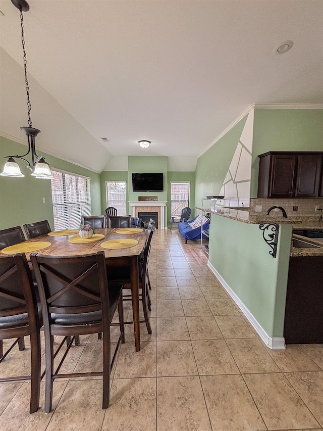 dining room featuring light tile patterned floors, visible vents, vaulted ceiling, a tiled fireplace, and crown molding