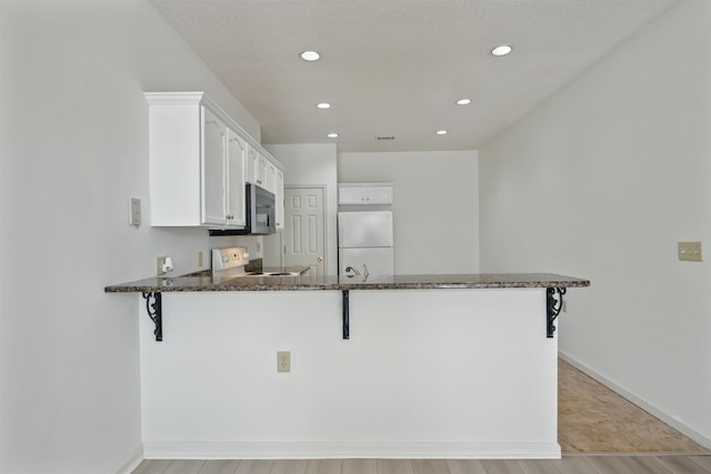 kitchen featuring a peninsula, stove, freestanding refrigerator, stainless steel microwave, and dark stone countertops