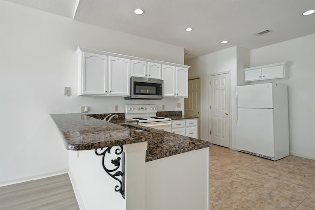 kitchen featuring a peninsula, white appliances, visible vents, white cabinets, and dark stone countertops