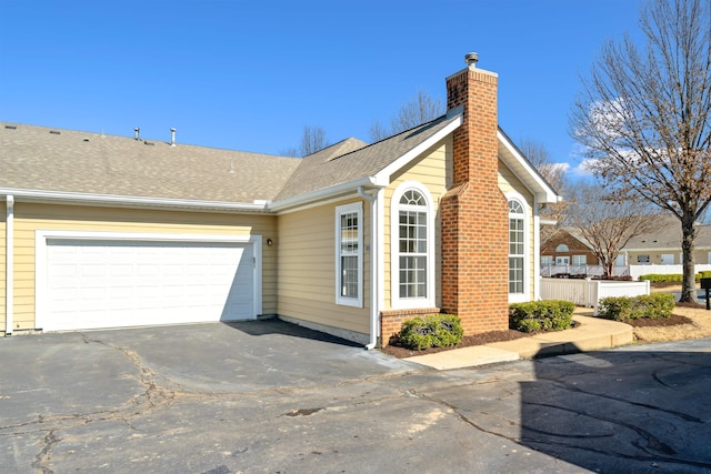 view of side of home with driveway, a shingled roof, a chimney, and an attached garage