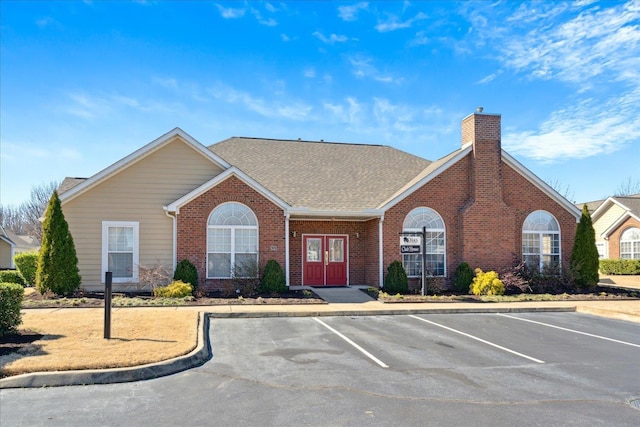 view of front of property featuring uncovered parking, brick siding, a chimney, and a shingled roof