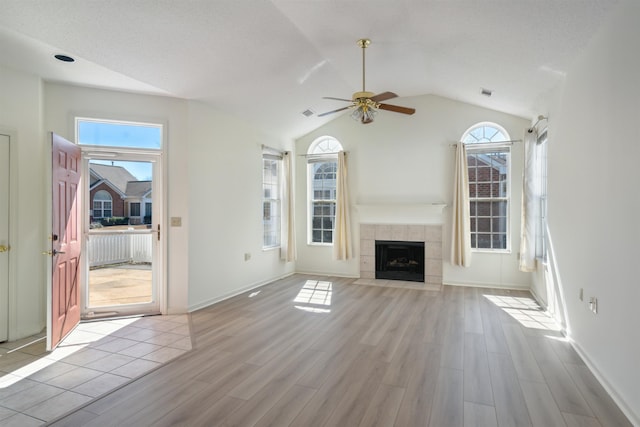 unfurnished living room with lofted ceiling, a tile fireplace, wood finished floors, a ceiling fan, and baseboards